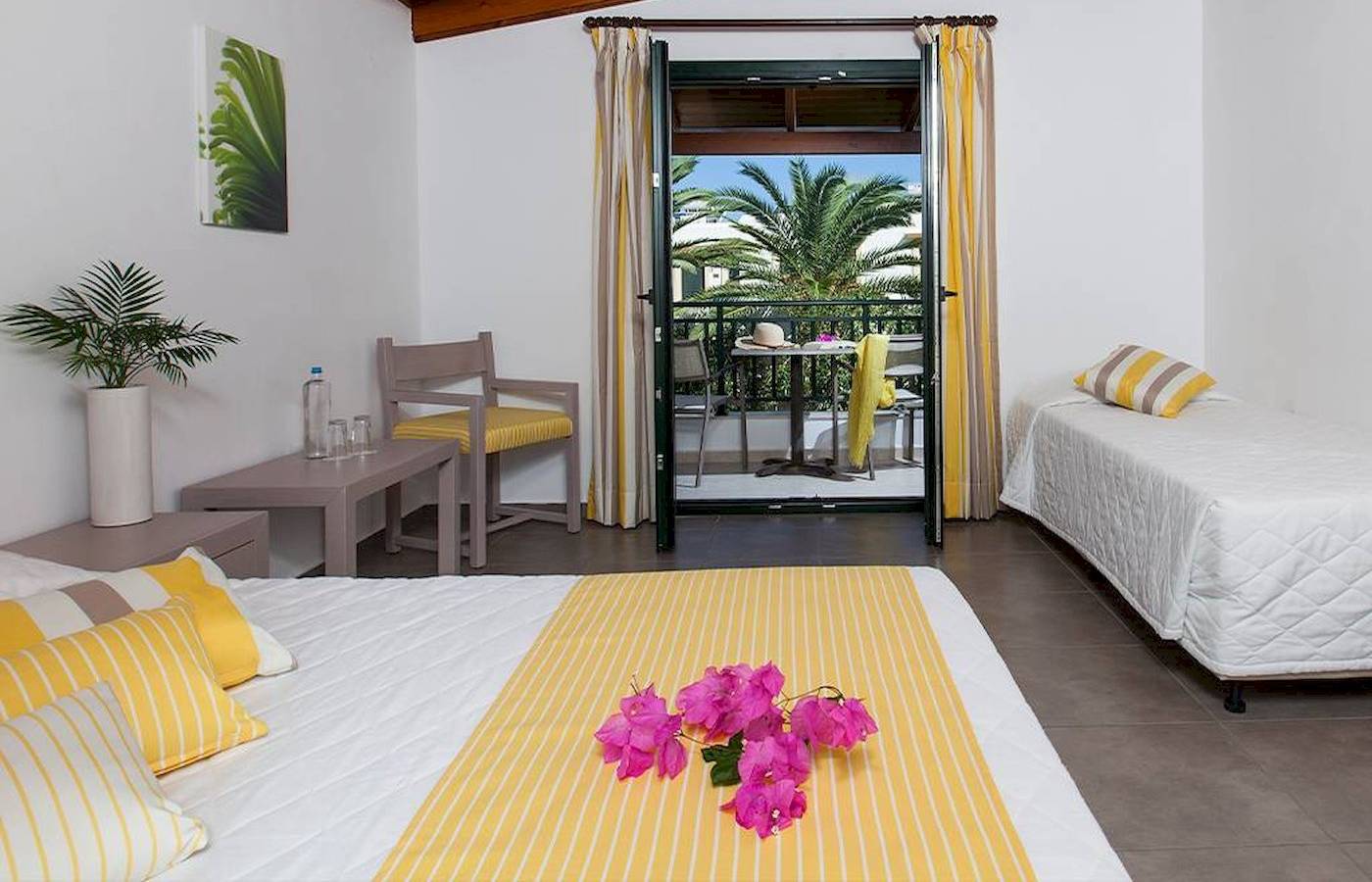 Schlafzimmer im Chrissi Amoudia Hotel mit zwei Betten, Balkon und Palmenblick.