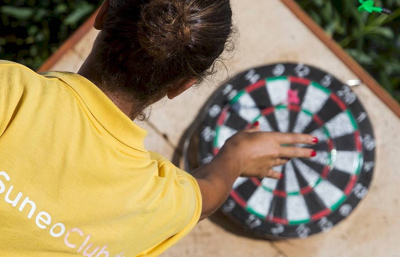 Eine Frau in einem gelben Suneo-Club-T-Shirt spielt Dart im Freien beim Chrissi-Amouida-Hotel.