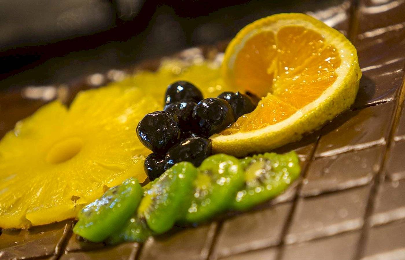 Nahaufnahme einer Schokoladenplatte mit Ananas, Kiwi, Blaubeeren und Orangenscheibe im Chrissi Amoudia Hotel.