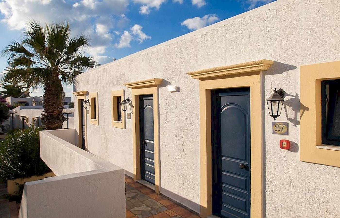 Eingangsbereich des Chrissi Amoudia Hotels mit weißen Wänden, blauen Türen und einer Palme