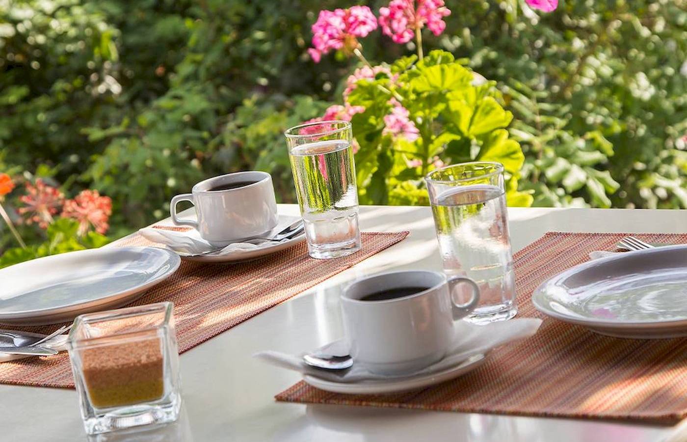 Frühstückstisch im Garten des Chrissi Amoudia Hotels mit Kaffee, Wasser und Gebäck.