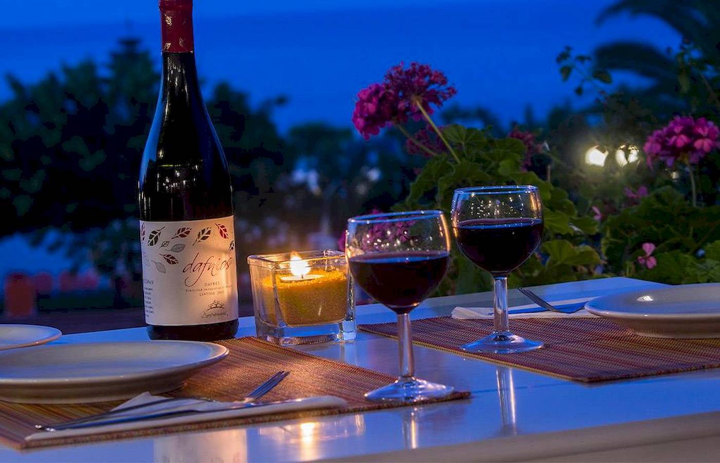 Romantisches Dinner im Hotel Chrissi Amoudia mit Weinflasche, Kerzen und Gläsern auf einer Tischplatte.