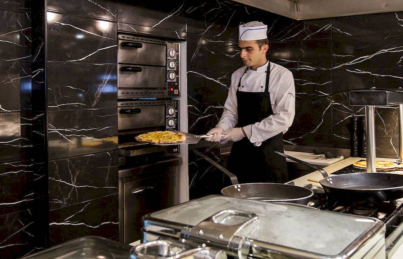 Koch im Chrissi Amoudia Hotel zieht Pizza aus dem Ofen