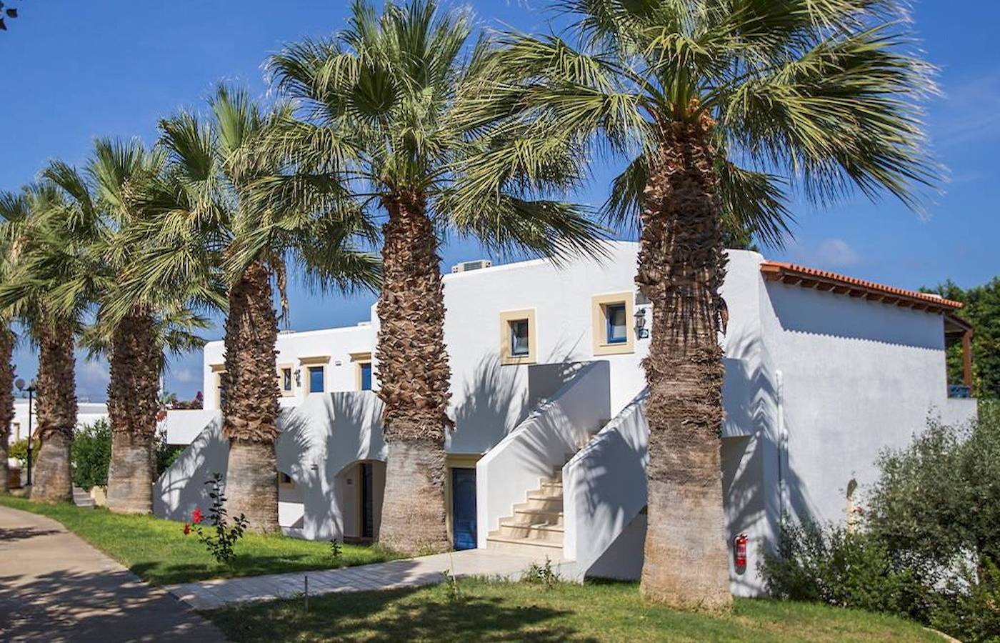 Außenansicht des Chrissi Amoudia Hotels mit weißen Gebäuden und Palmen.