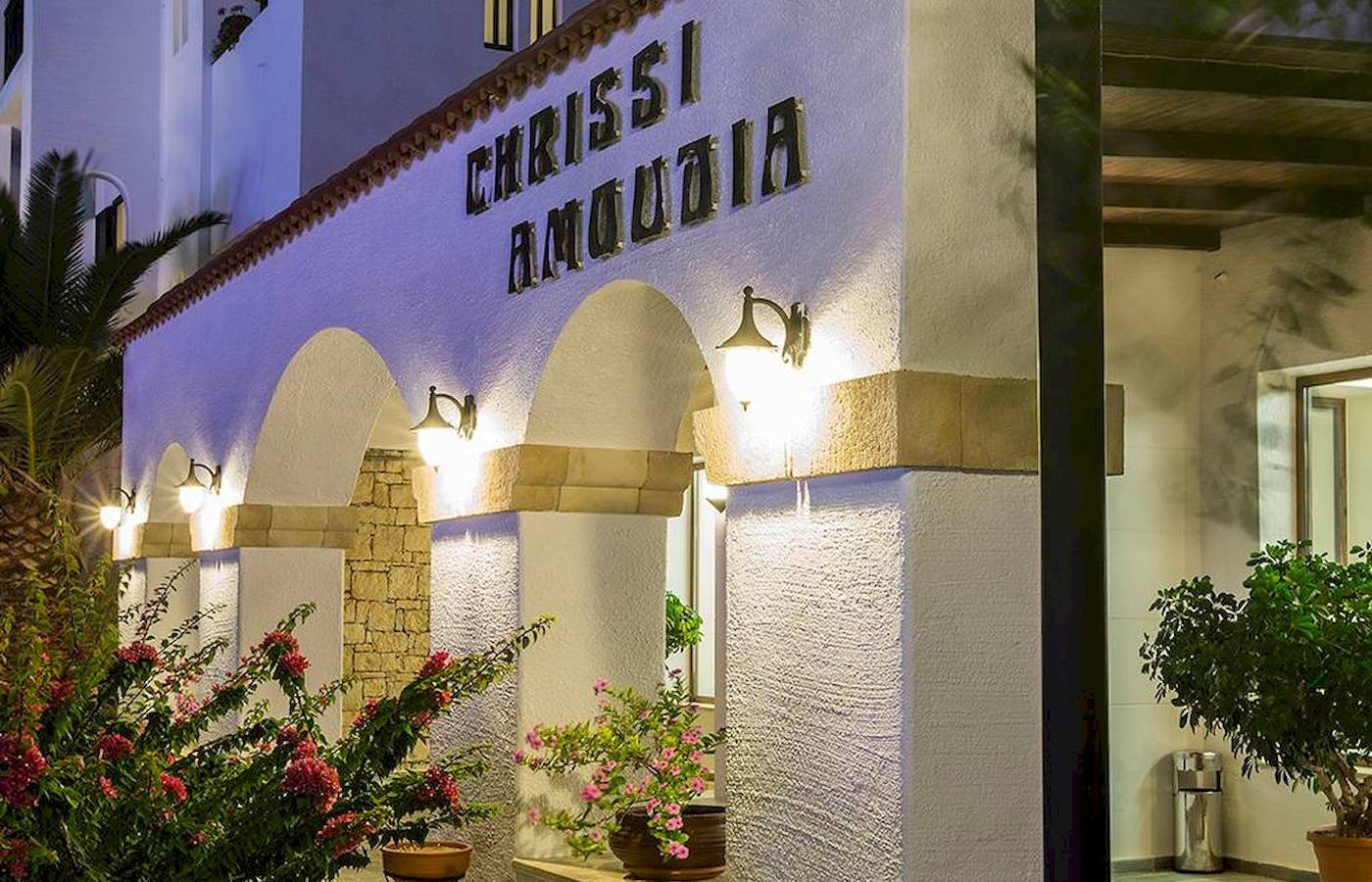 Das Chrissi Amoudia Hotel mit beleuchtetem Eingang und Pflanzen davor.
