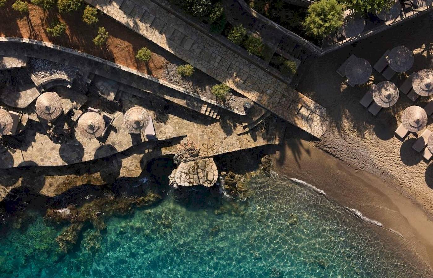 Luftaufnahme des Minos Palace Hotel & Suites am Strand mit Palmen und Sonnenschirmen.