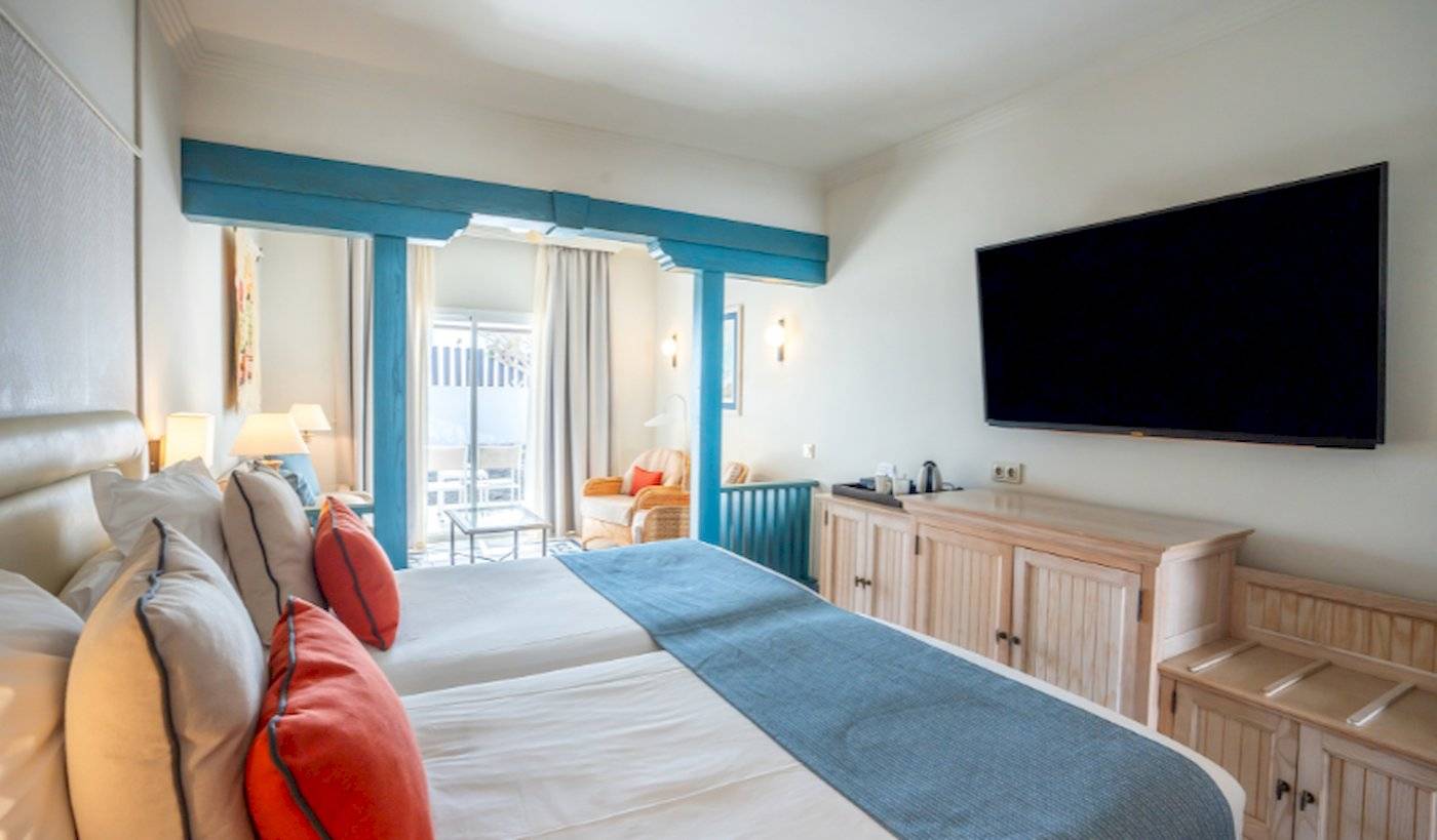 Innenansicht eines Doppelzimmers im LIVVO Volcan Lanzarote Hotel mit zwei Betten, Fernseher, Schränken und einer Veranda.
