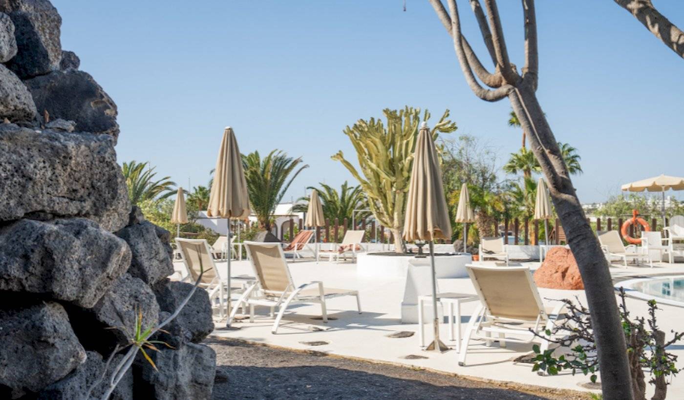 Pool-Lounge-Bereich im LIVVO Volcan Lanzarote Hotel mit Sonnenliegen, Sonnenschirmen und Pflanzen.