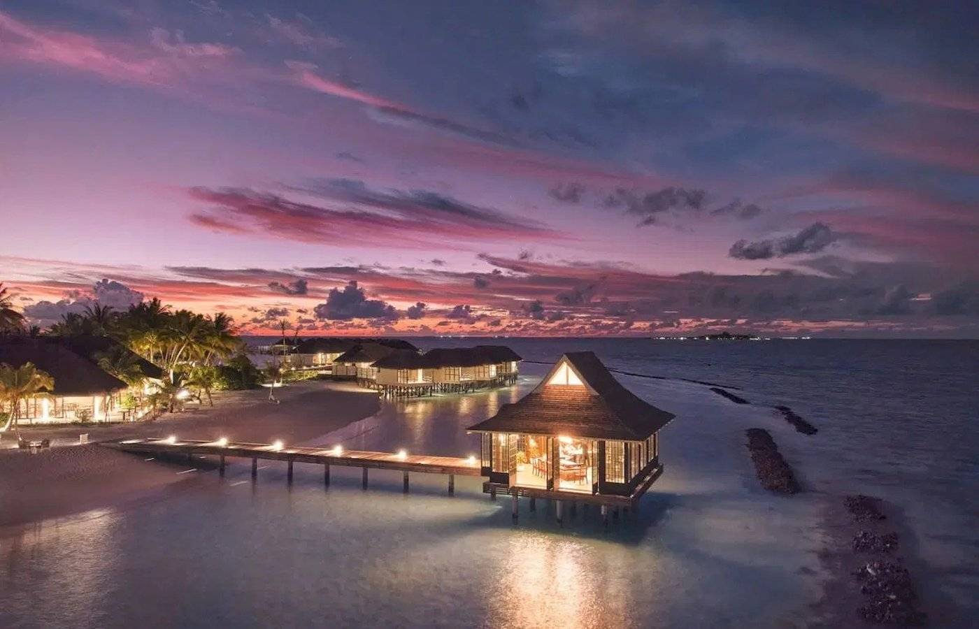 Nova Maldives Hotel bei Sonnenuntergang mit Blick auf das Meer und mehrere Wasservillen