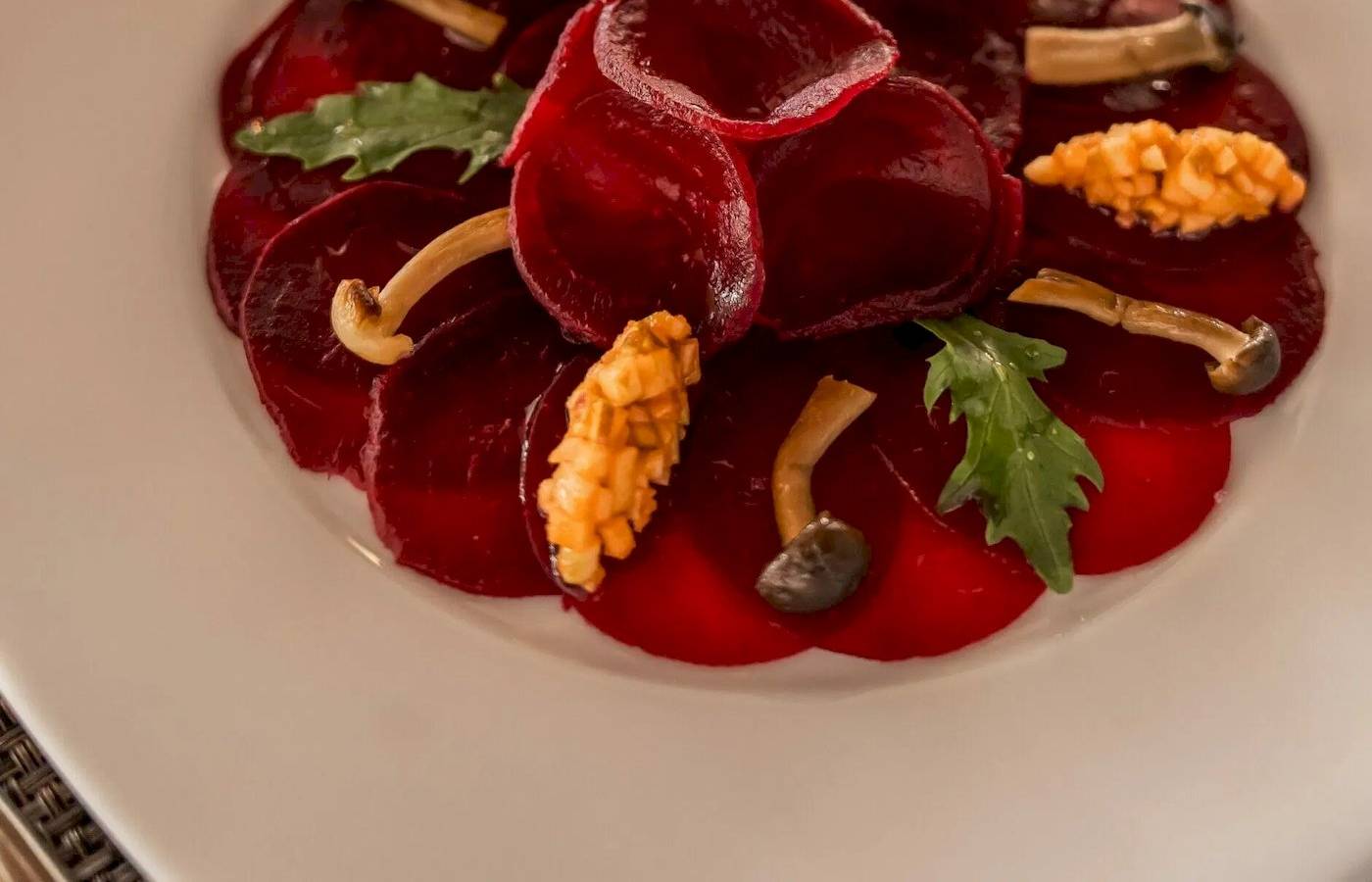 Ein weißer Teller mit einem Salat aus roten Rüben, Pilzen und grünen Blättern.