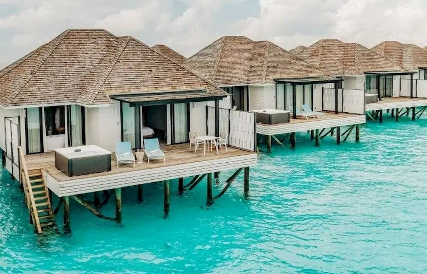 Reihe von Wasservillen im Nova Maldives Hotel mit blauem Wasser und blauem Himmel.