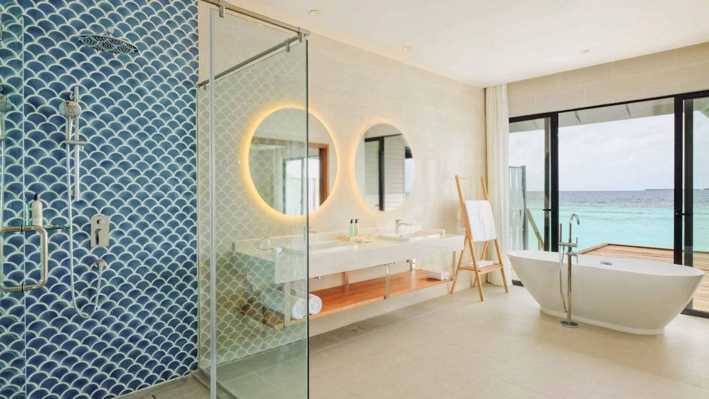 Badezimmer im Nova Maldives Hotel mit Meerblick, Badewanne, zwei Waschbecken und einer Dusche.