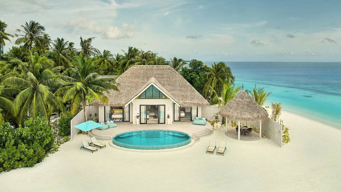 Luftaufnahme des Nova Maldives Resorts mit einer privaten Villa, Swimmingpool und Sonnenliegen am Strand.