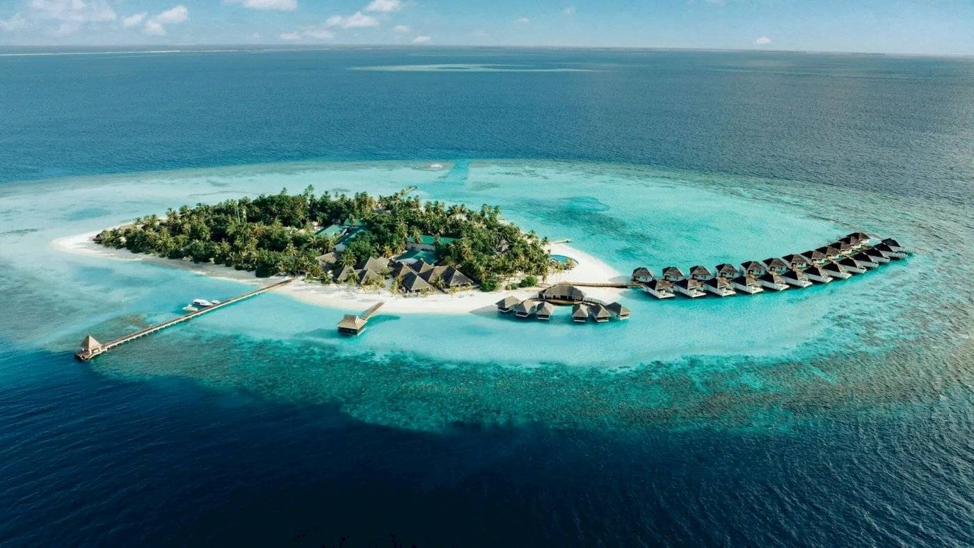 Luftaufnahme der Nova Maldives Insel mit vielen Wasserbungalows und einem Steg.