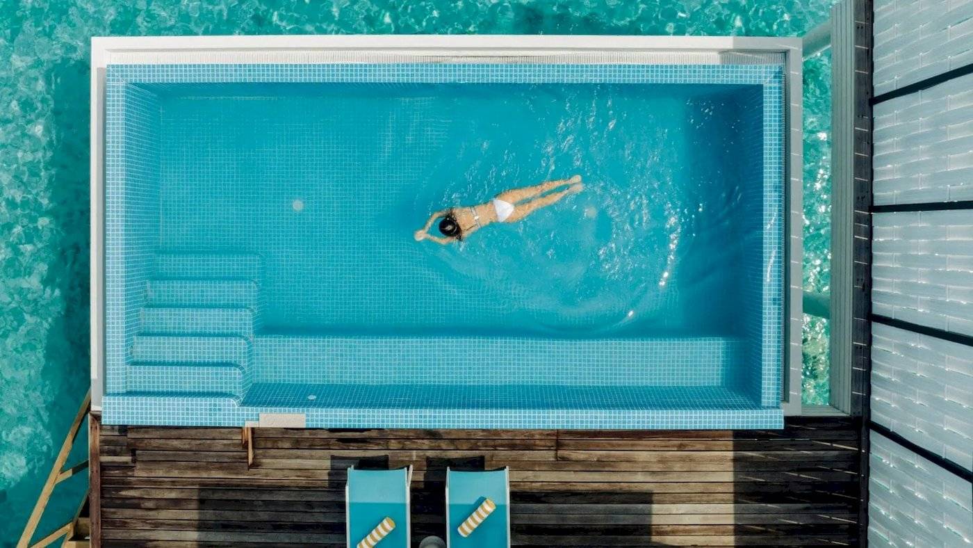 Ueberblick des Schwimmbeckens im Nova Maldives Hotel mit einer Frau, die schwimmt.