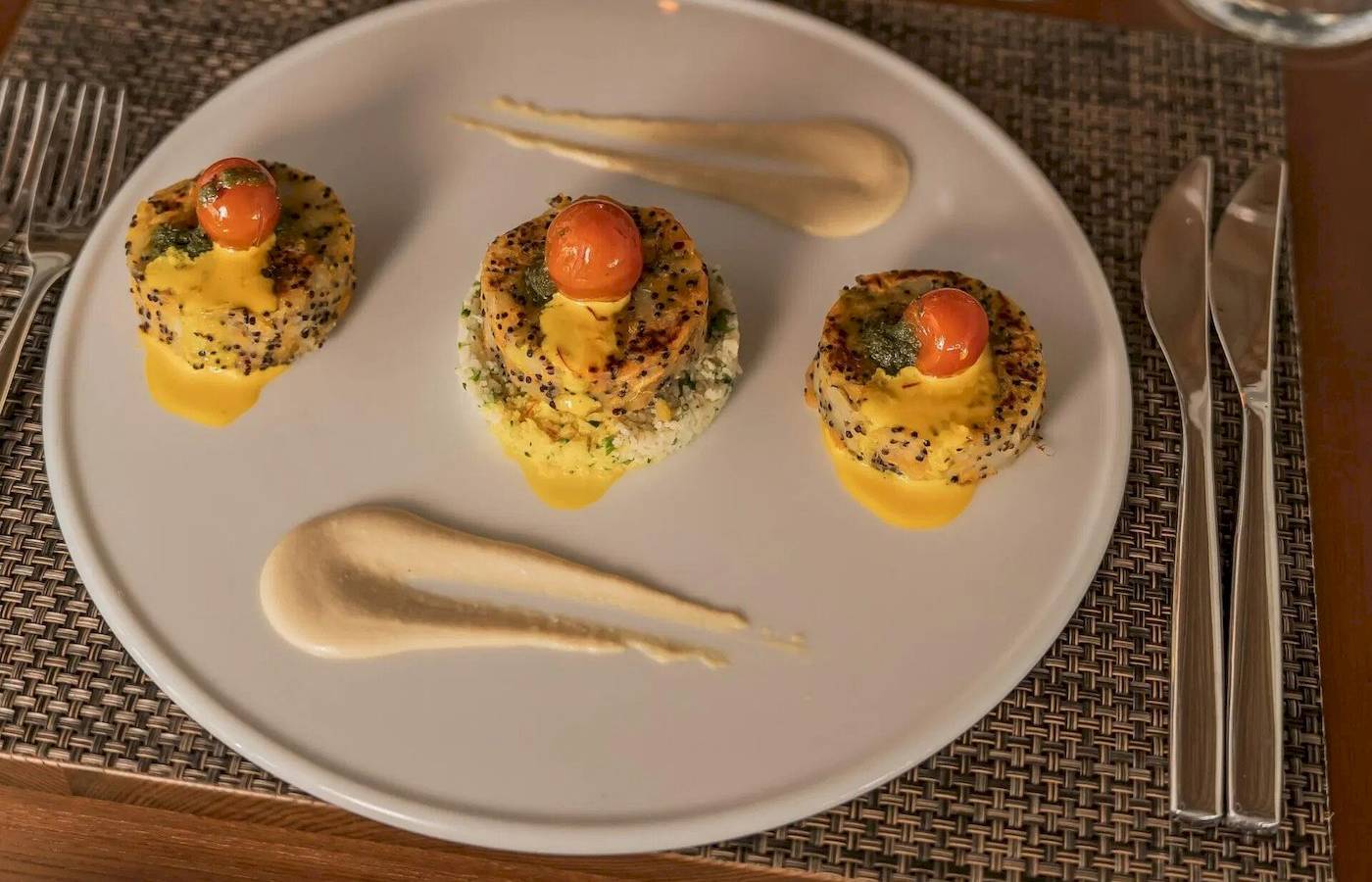 Speiseplatte mit drei runden Gerichten auf weißem Teller, serviert mit Besteck und Glas auf einem Tisch.