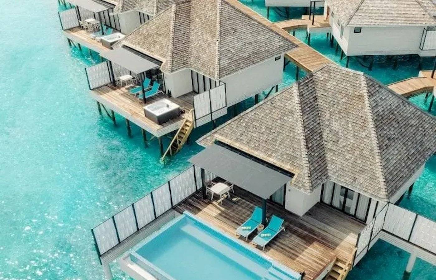 Aus der Luft aufgenommene Nova Maldives Wasservillen mit blauem Pool und Lounge-Bereich.