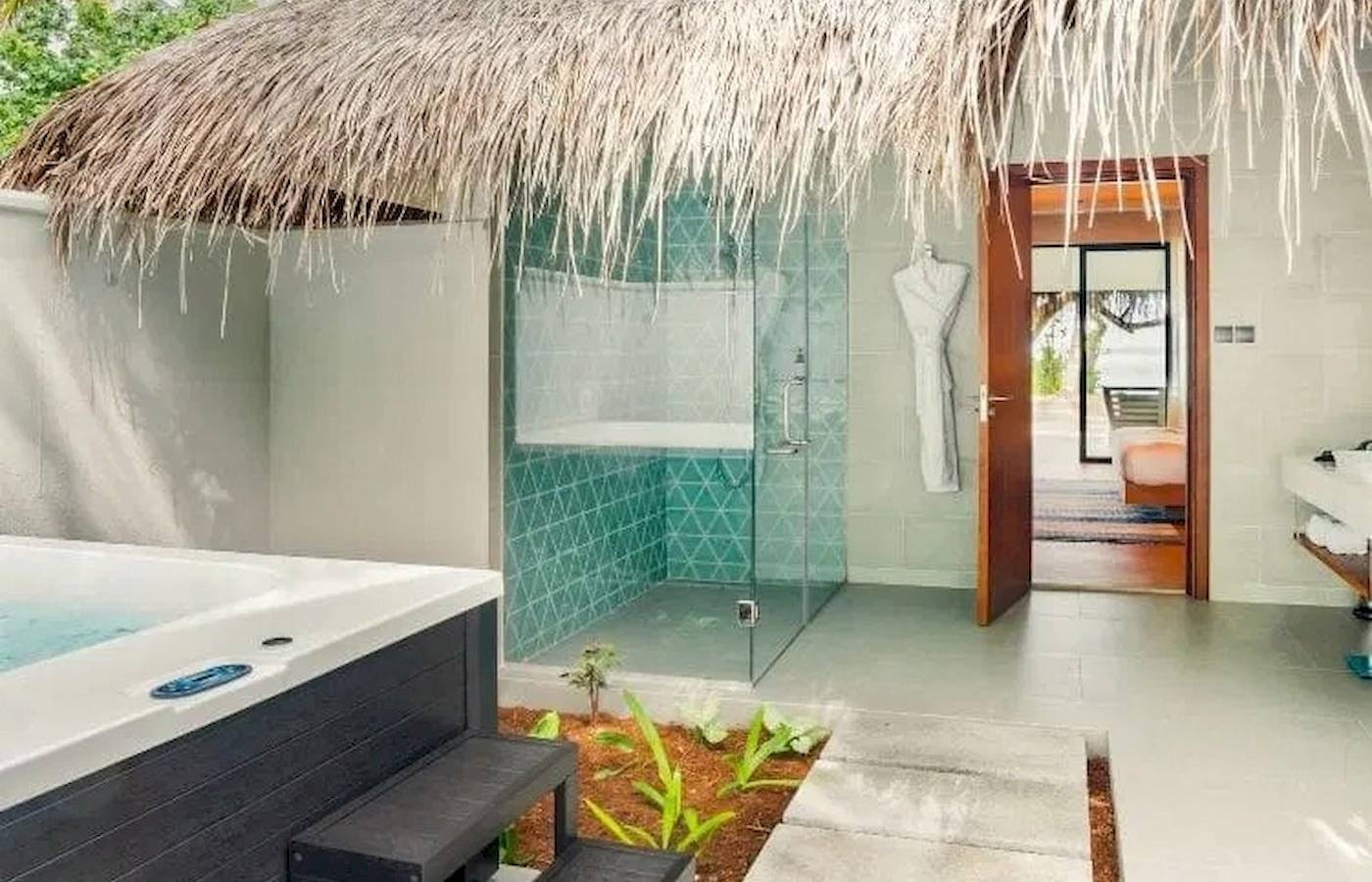 Außenbereich des Nova Maldives Hotels mit Jacuzzi und Duschbereich unter einem Strohhutdach.