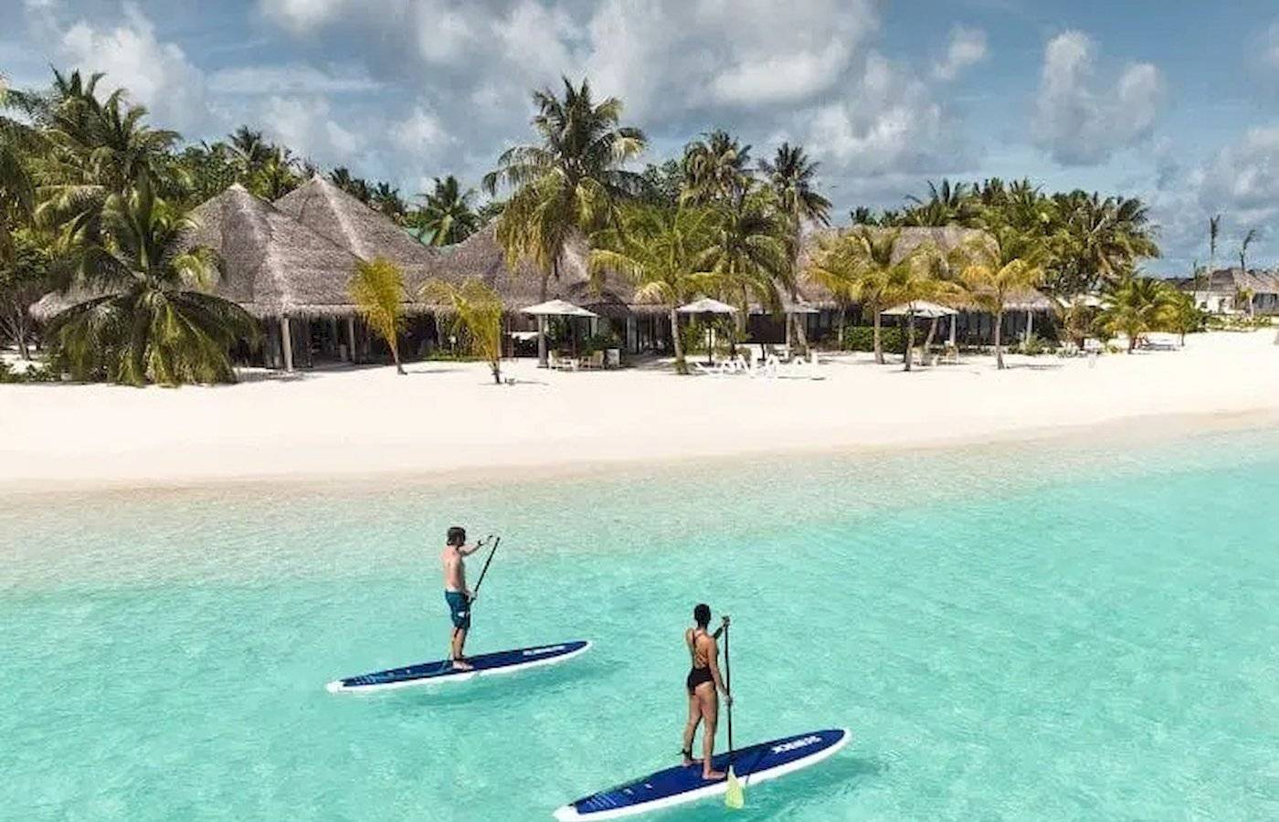 Zwei Personen paddeln auf blauen Brettern im klaren Wasser vor Nova Maldives.