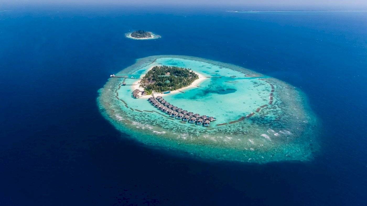 Luftaufnahme der Nova Maldives Insel mit Wasserbungalows und blauem Wasser