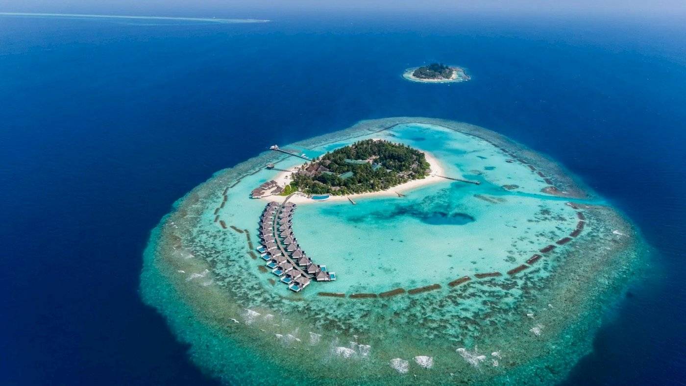 Luftaufnahme des Nova Maldives Resorts, zeigt die Insel mit Wasservillen und blauem Meer.