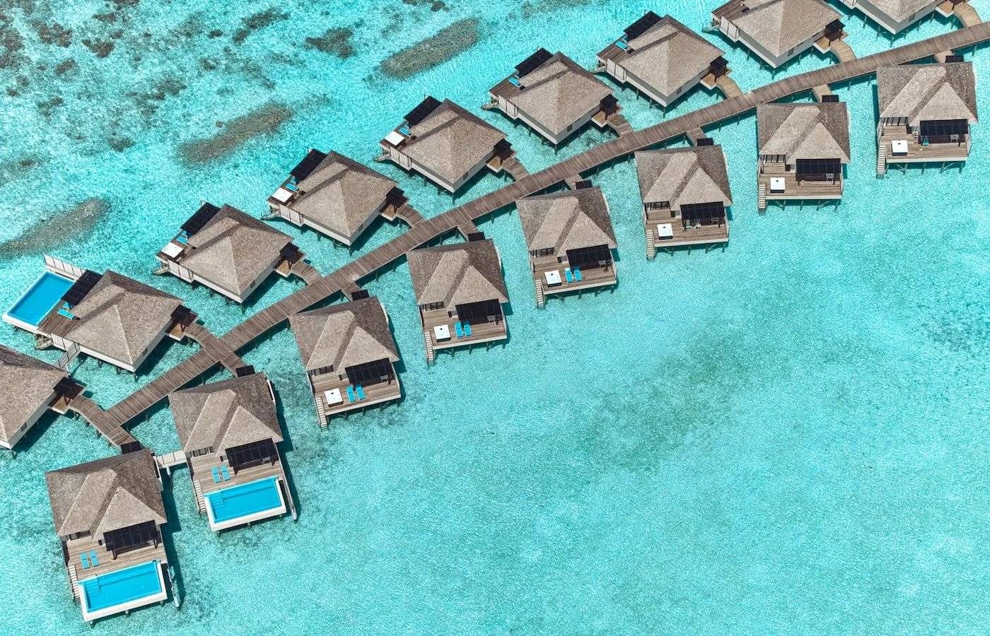 Luftaufnahme des Nova Maldives Resorts mit Wasservillen und Stegen