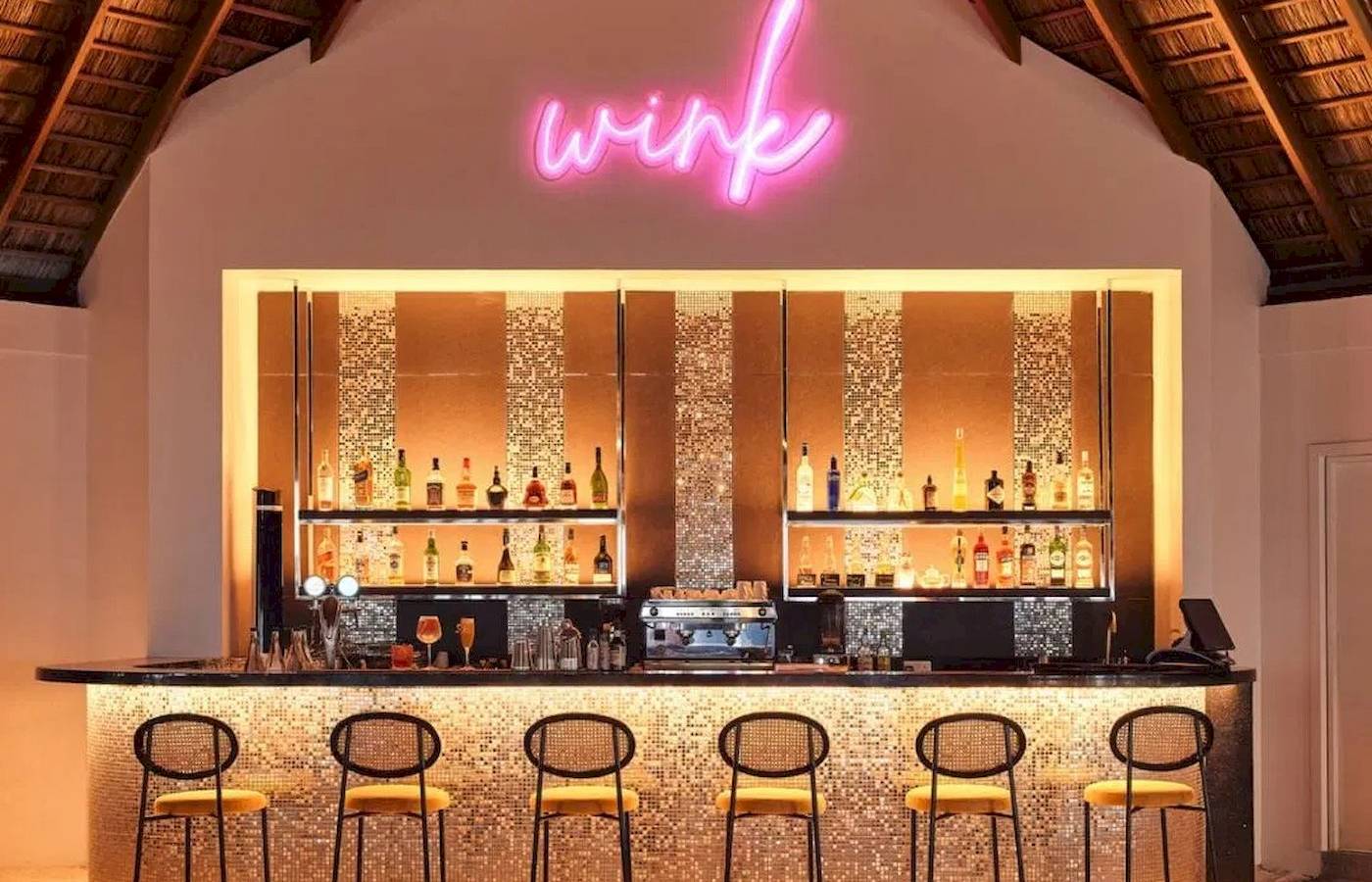 Bar im Nova Maldives Hotel mit leuchtendem Wink-Schild und gefüllten Regalen