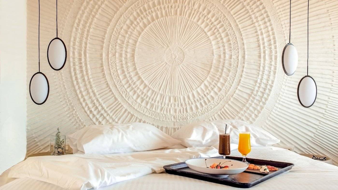 Bett im Mitsis Selection Rinela Hotel mit Frühstückstablett und Getränken