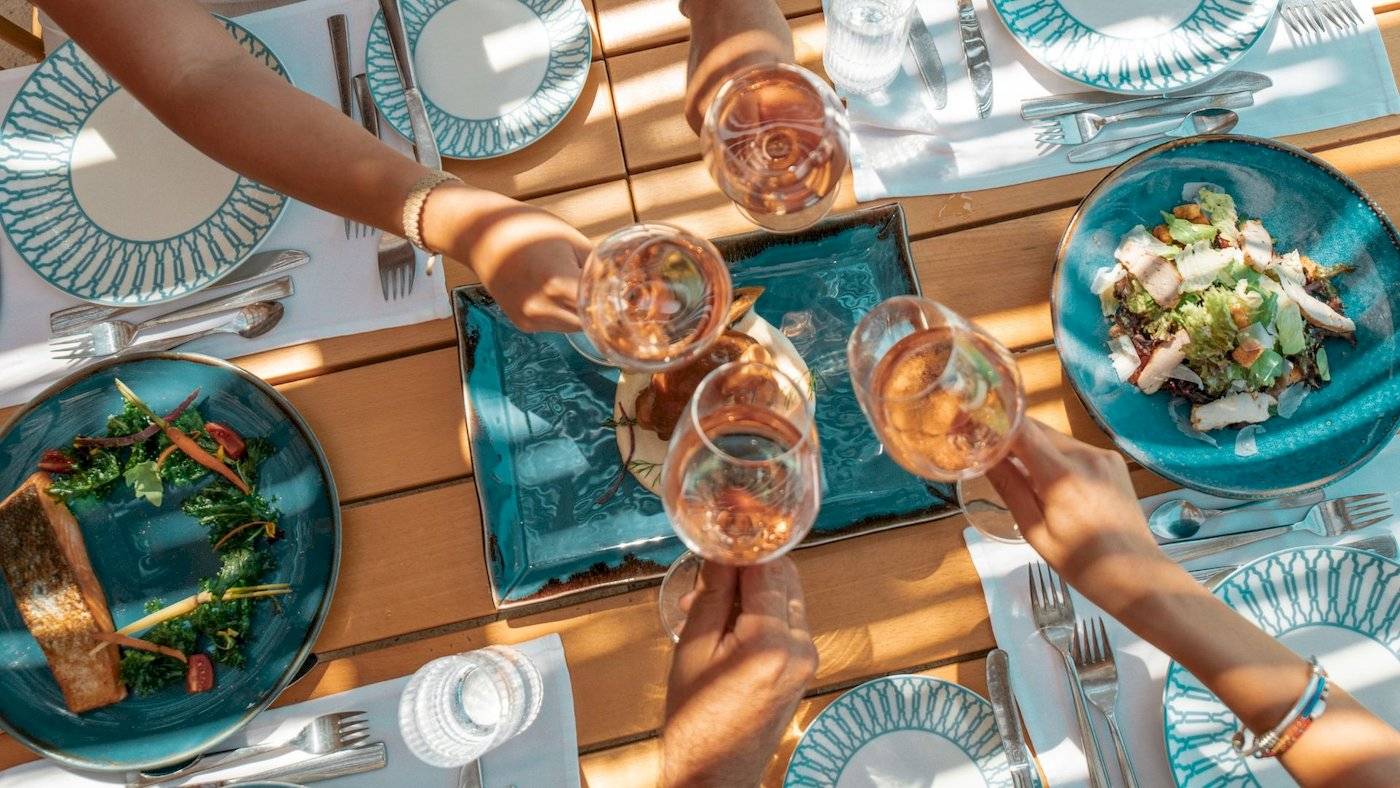 Mehrere Haende mit Weingläsern über einem Frühstückstisch im Mitsis Selection Rinela Hotel.