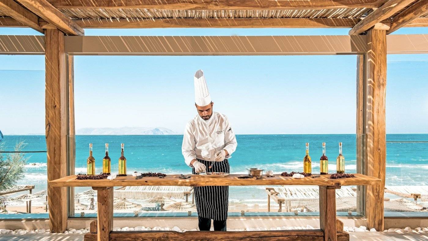 Koch in Mitsis Selection Rinela bereitet Essen zu, Blick auf das Meer