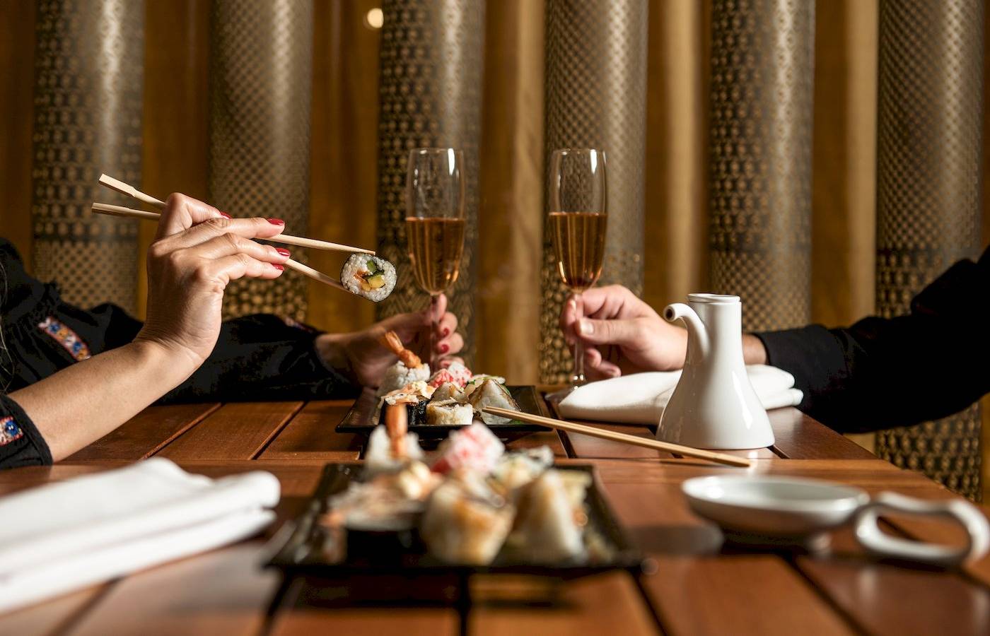 Zwei Personen sitzen an einem Tisch und essen Sushi mit Chopsticks und trinken Champagner.