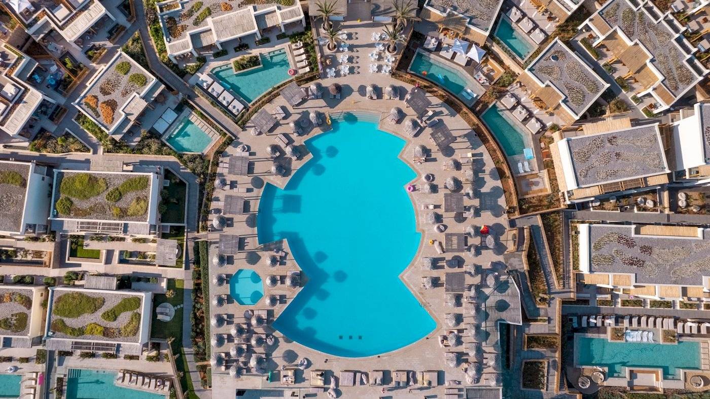 Luftaufnahme des Mitsis Selection Rinela Hotels mit mehreren Pools und Liegebereichen.