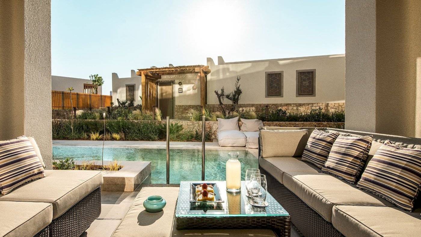 Außenbereich des Mitsis Selection Rinela Hotels mit Loungemöbeln, Swimmingpool und Garten