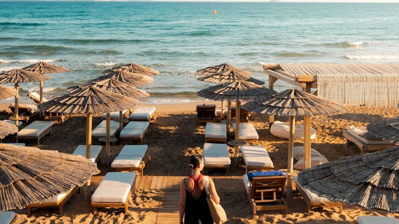 Eine Frau auf dem Strand des Mitsis Selection Rinela Hotels, umgeben von Liegen und Sonnenschirmen.