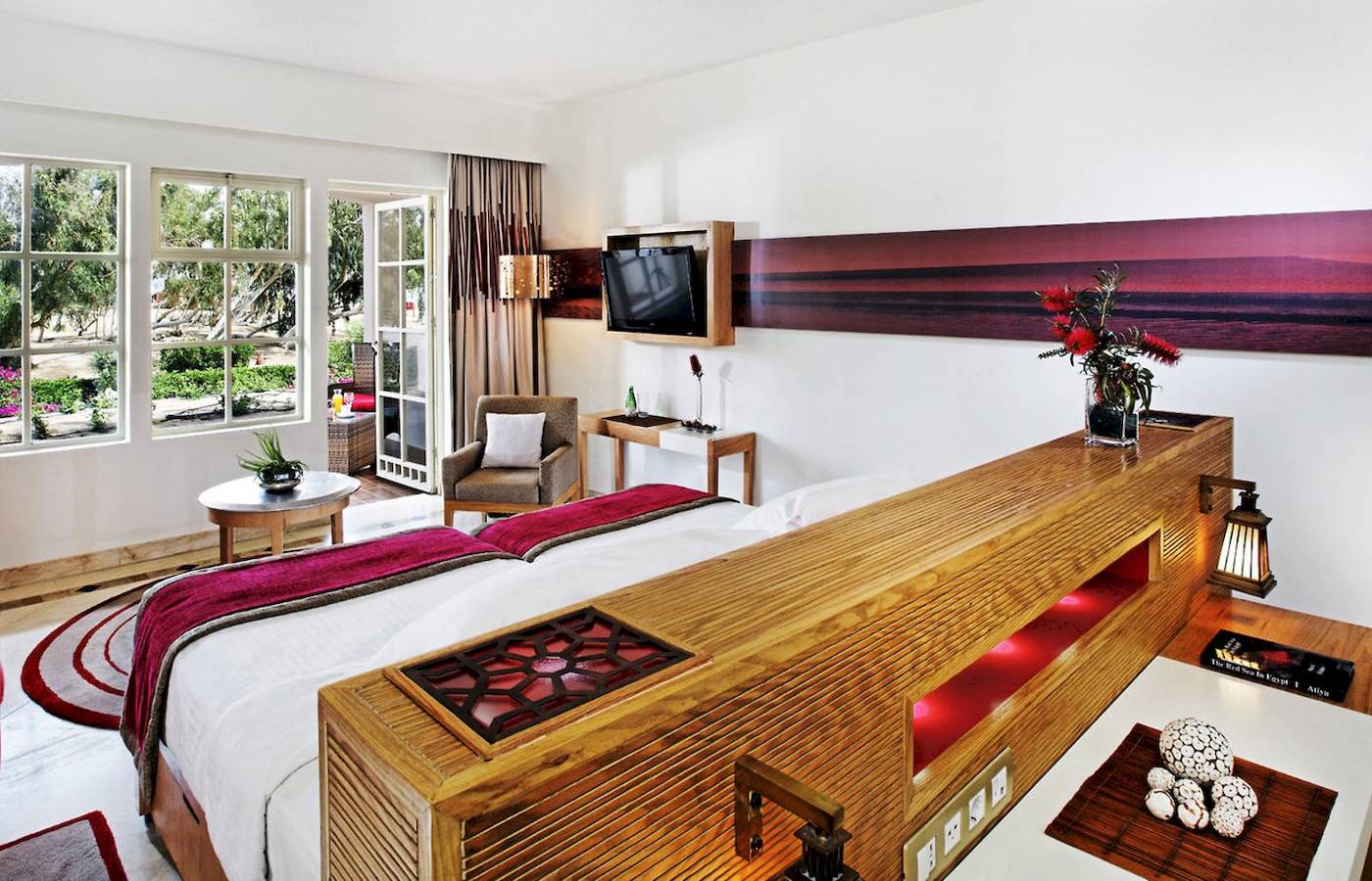 Innenansicht eines Hotelzimmers im Mövenpick Resort & Spa El Gouna mit einem Bett, Fernseher und Pflanzen.