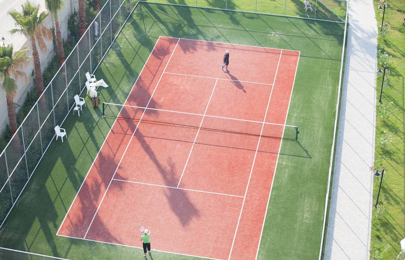 Zwei Personen spielen Tennis auf dem Tennisplatz im Freien im Defne Defnem Hotel.