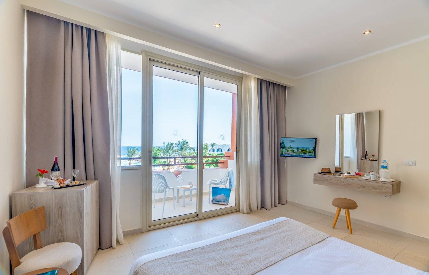 Innenansicht eines Zimmers im Three Corners Equinox Beach Resort mit Balkon, Fernseher und Blick auf den Ozean.