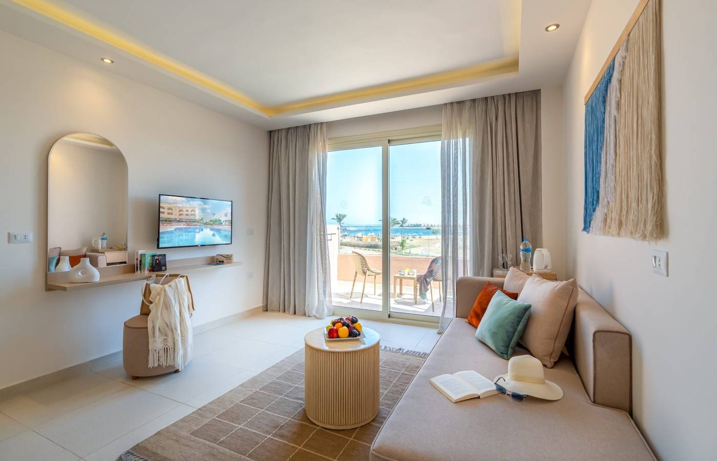 Luxuriöses Zimmer im Three Corners Equinox Beach Resort mit Meerblick, inklusive Wohnzimmer mit Sofa, Tisch, Fernseher, und Balkon.