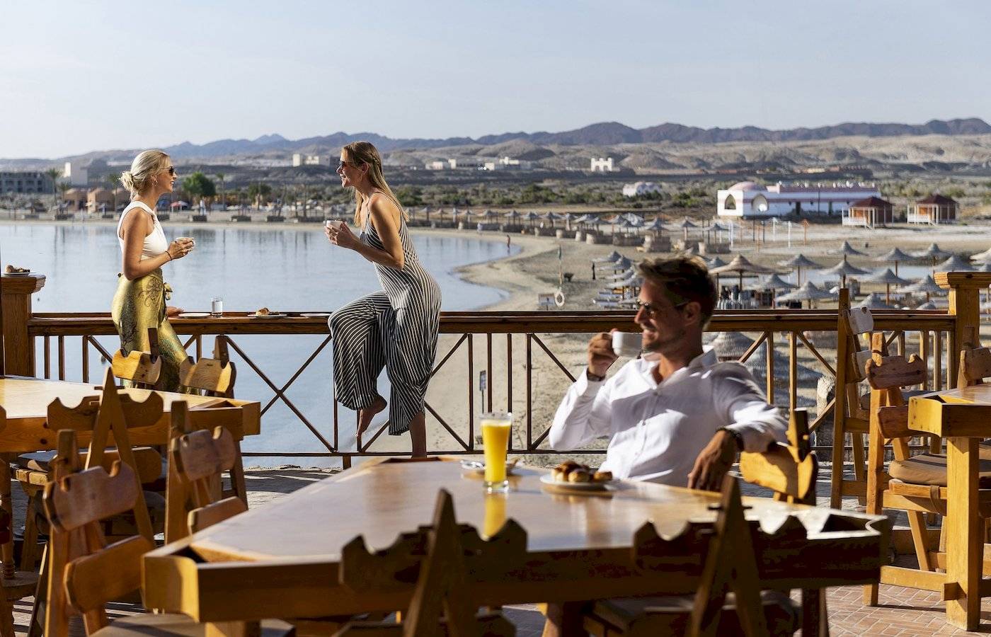 Drei Gäste sitzen auf der Terrasse des Three Corners Equinox Beach Resorts und genießen Getränke und Ausblick.