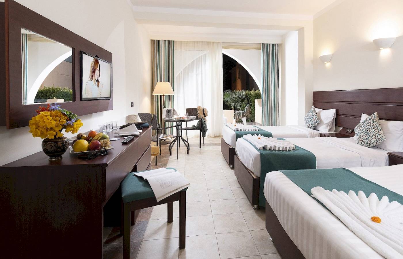 Drei Hotelzimmer im Three Corners Equinox Beach Resort mit Blumen, Obst und bequemen Betten.