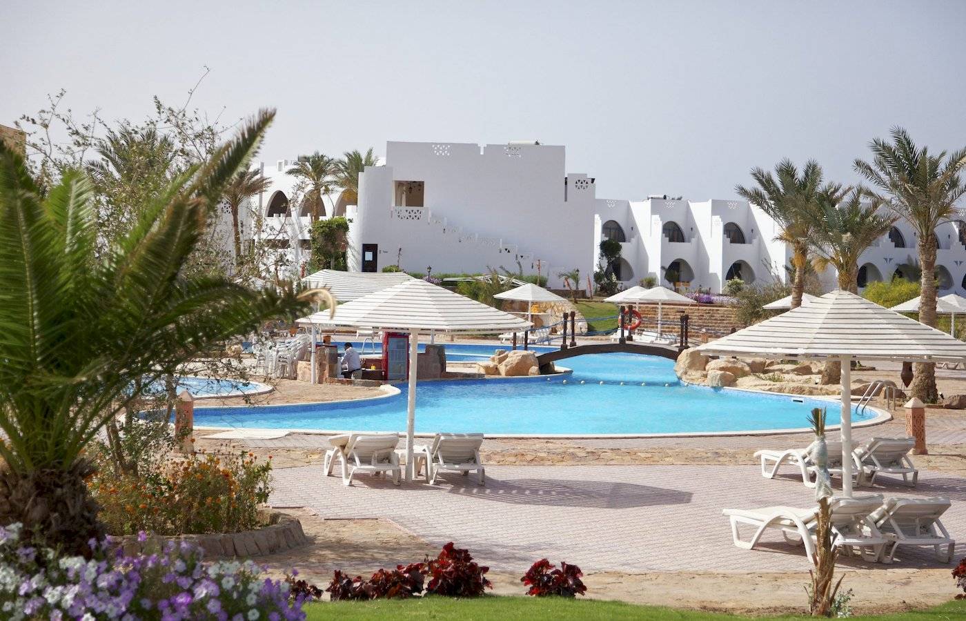 Ein Swimmingpool im Freien mit weißen Sonnenliegen und großen Sonnenschirmen im Three Corners Equinox Beach Resort.