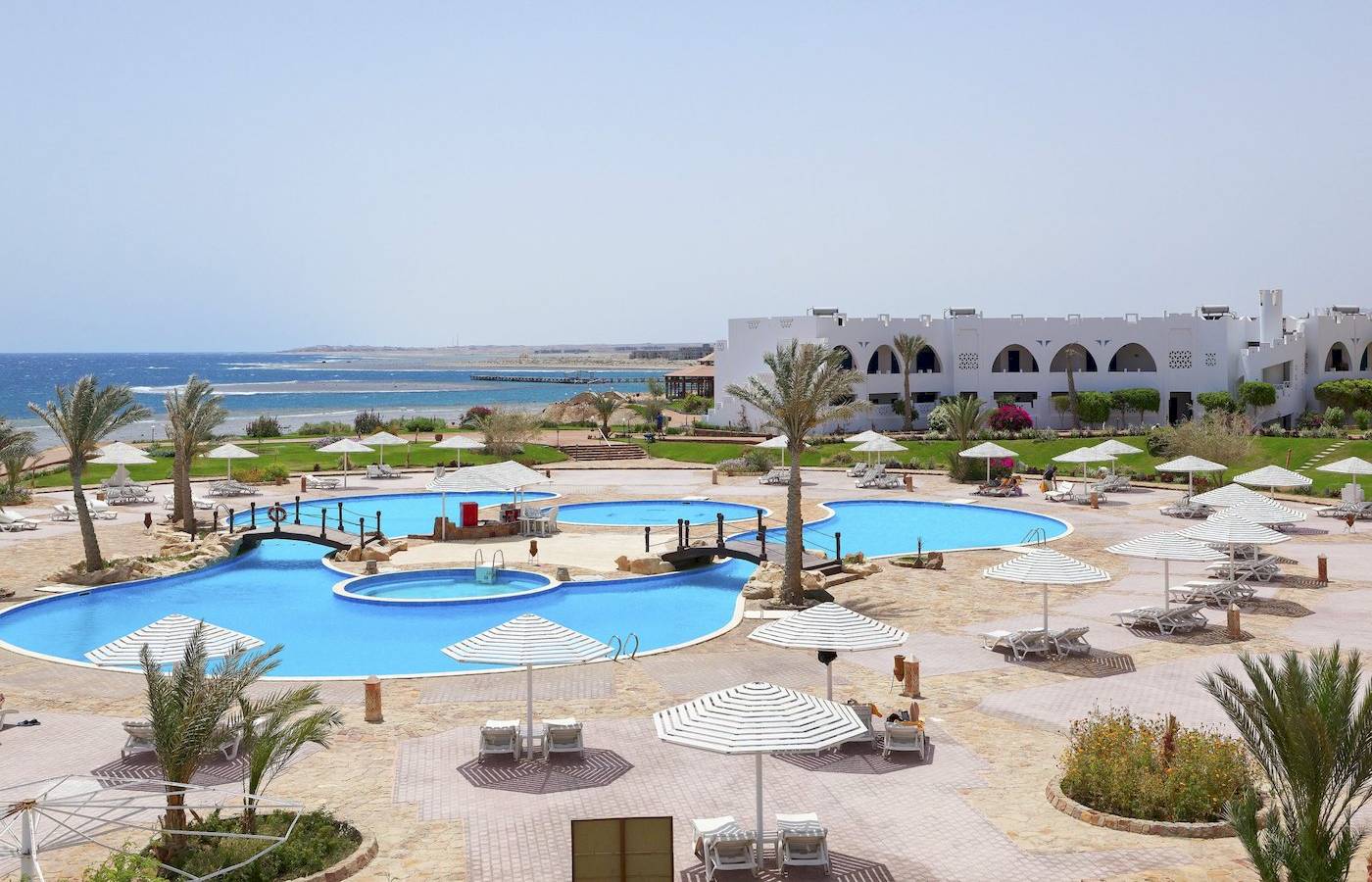 Luftaufnahme des Three Corners Equinox Beach Resorts mit Swimmingpools, Sonnenschirmen und Lounge-Stühlen.