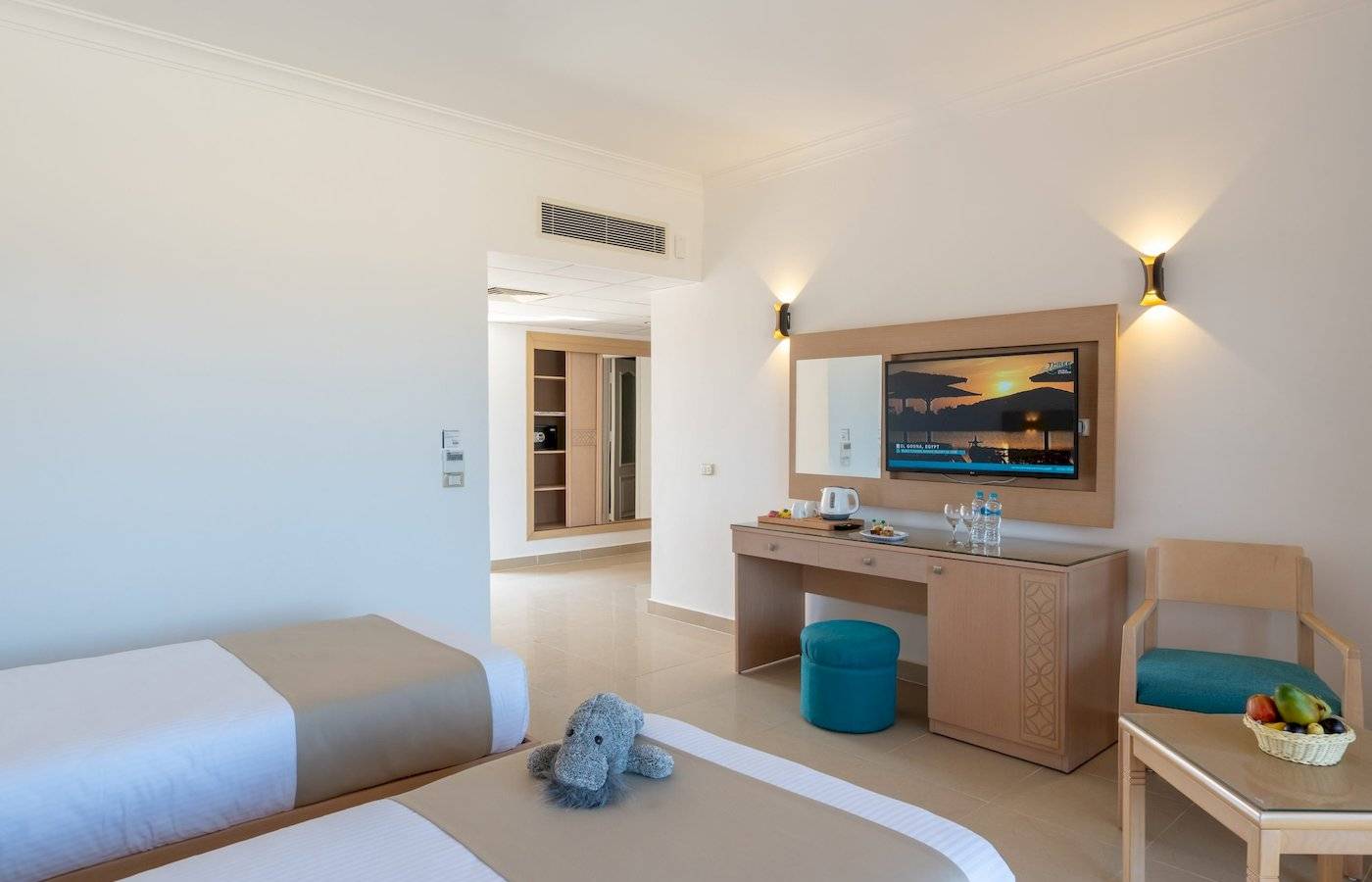 Zimmer im Three Corners Happy Life Beach Resort mit zwei Betten, Schreibtisch, Fernseher und Obstkorb.