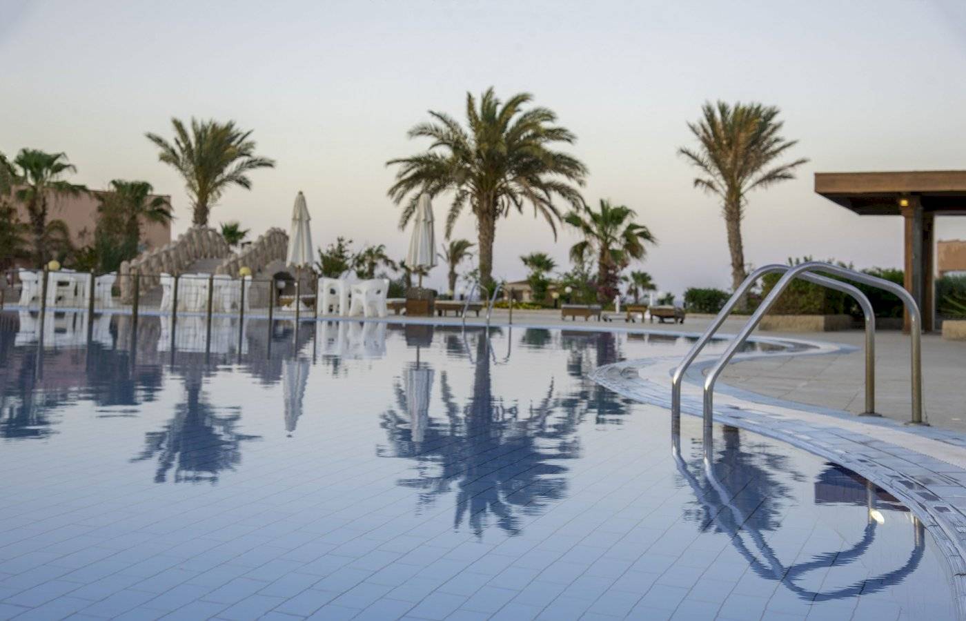 Schwimmbecken im Three Corners Happy Life Beach Resort mit Palmen und Sonnenliegen