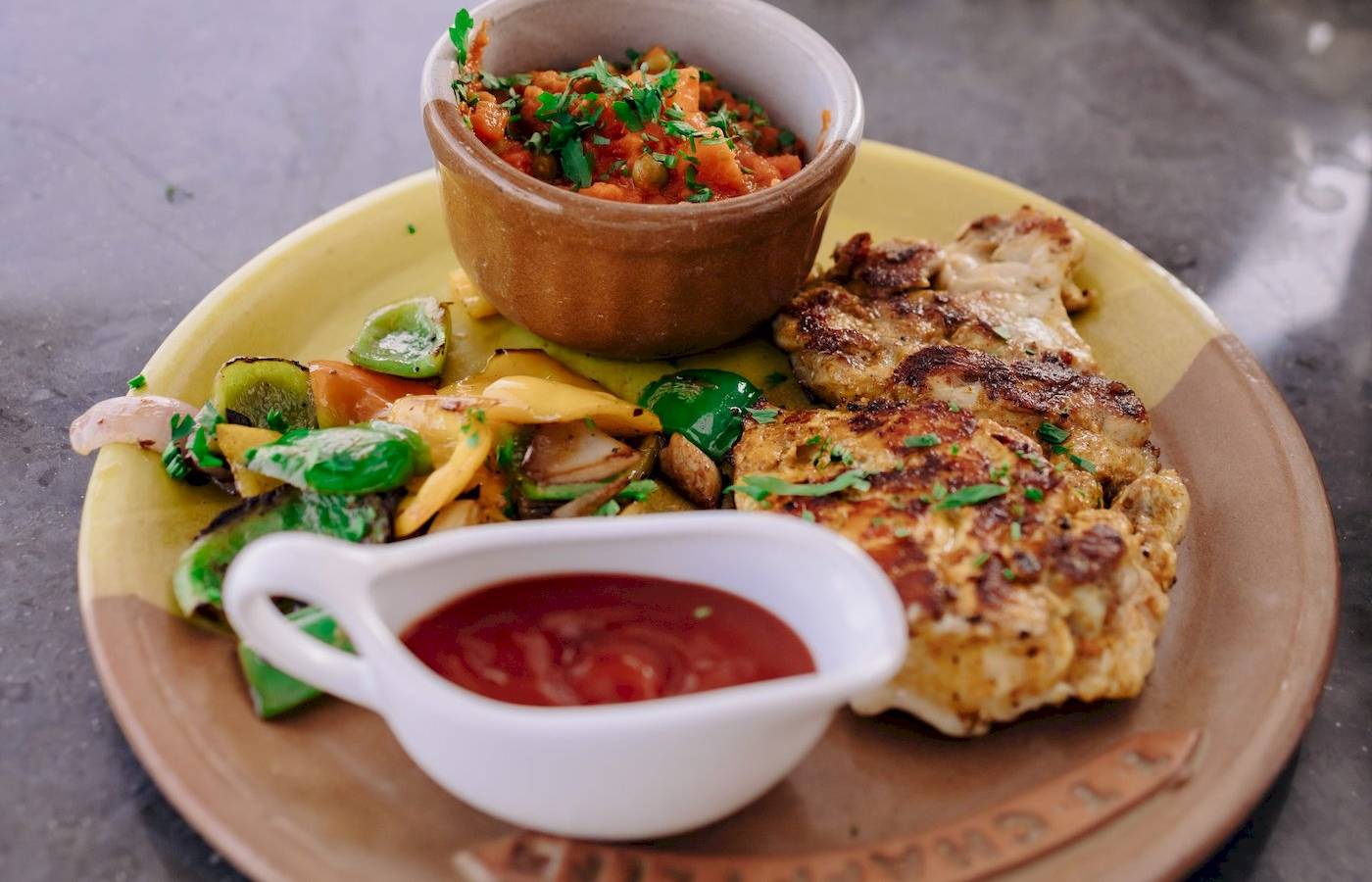 Ein Teller mit gegrilltem Fleisch, gemischten Gemüsen und einer Saucenschüssel.