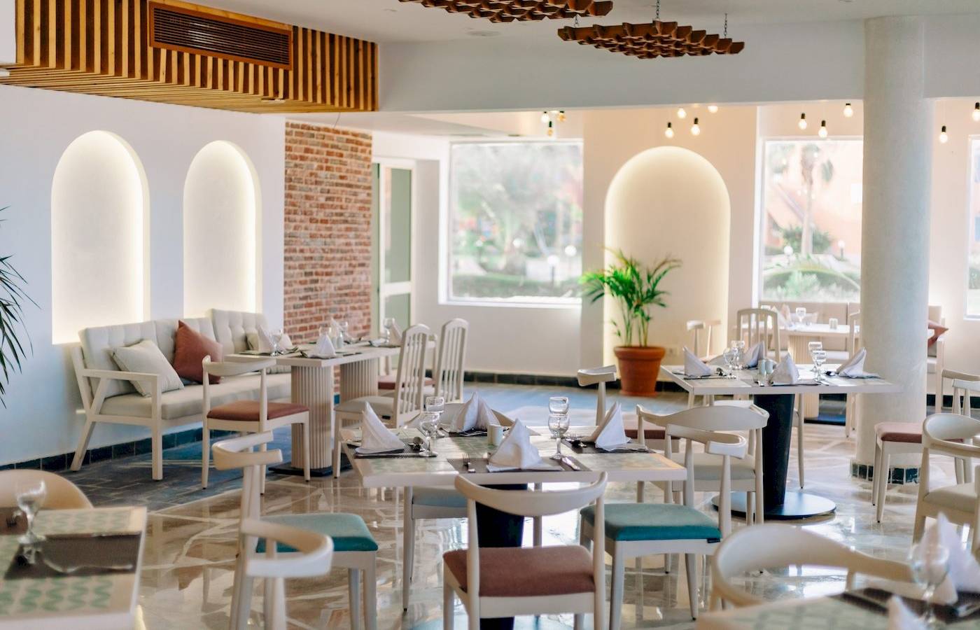 Innenansicht eines Restaurants im Three Corners Happy Life Beach Resort mit weißen Tischen und Stühlen.