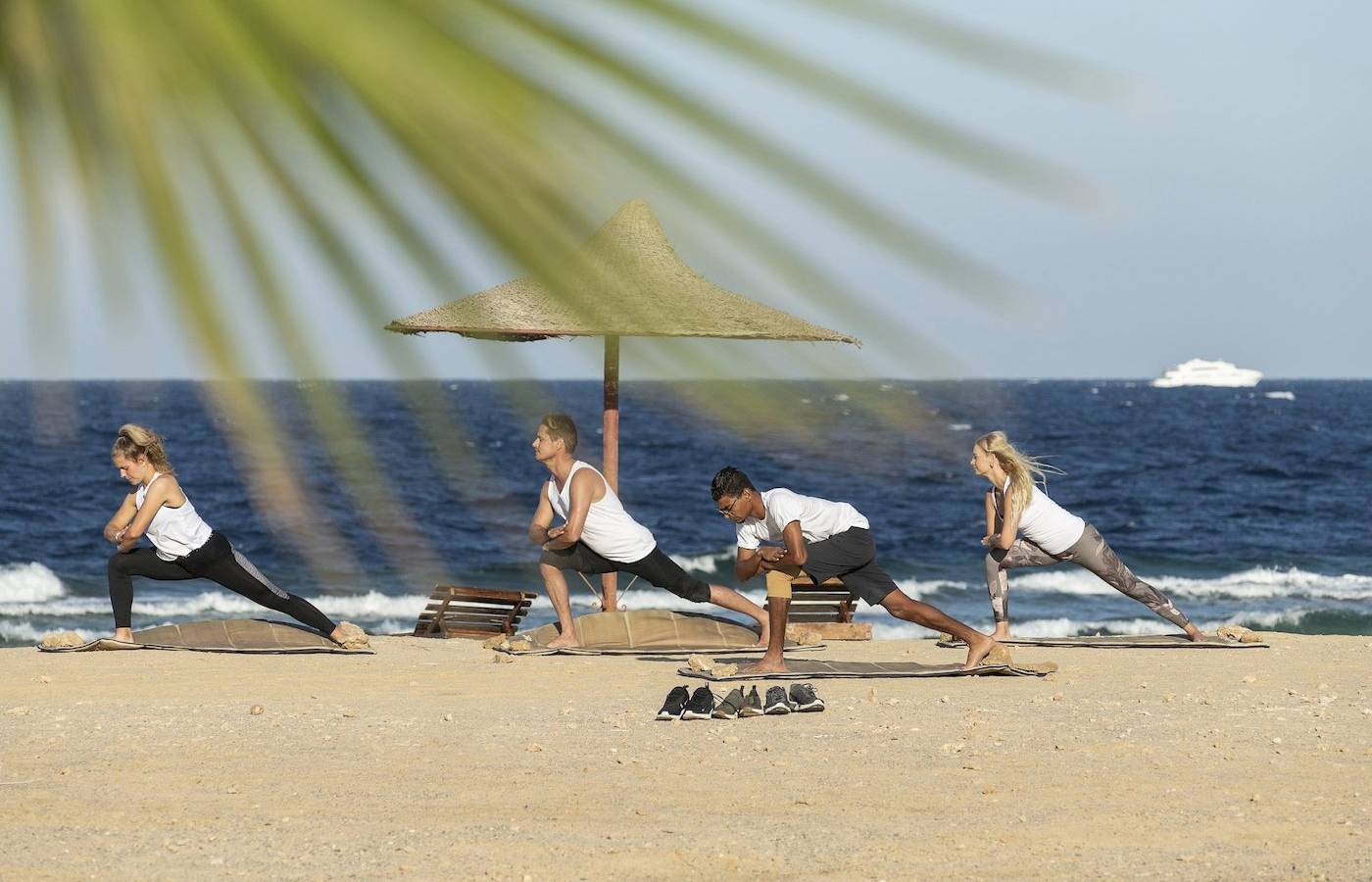 Gruppe von Menschen, die Yoga auf dem Strand unter einem Sonnenschirm machen.