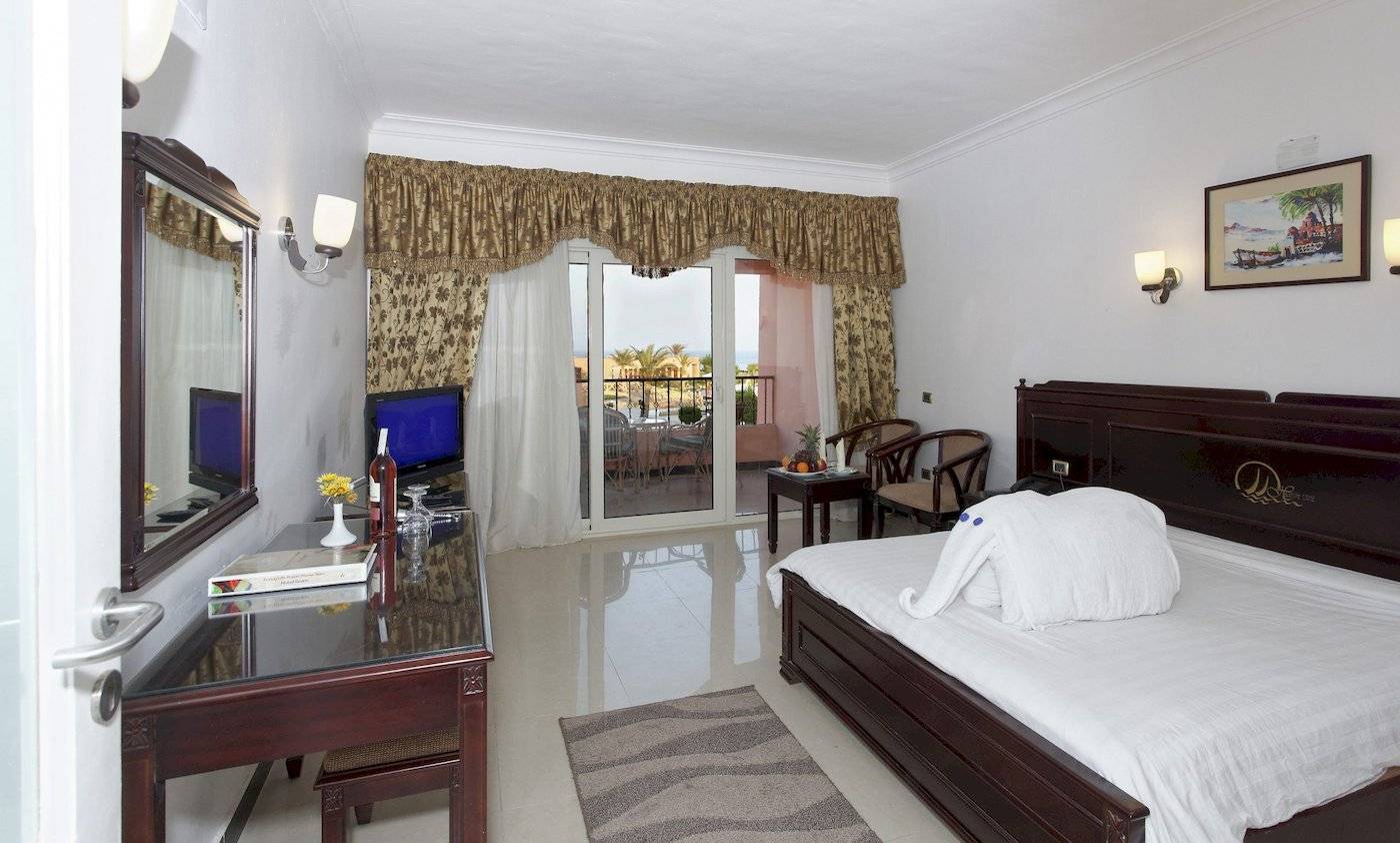 Ein Hotelzimmer im Three Corners Happy Life Beach Resort mit einem Bett, Fernseher, Tisch und einem Balkon.