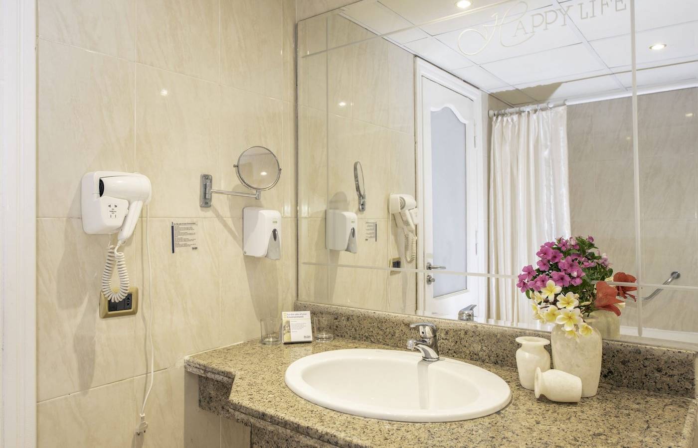 Badezimmer im Three Corners Happy Life Beach Resort mit Spiegel, Waschbecken und Blumenvase.