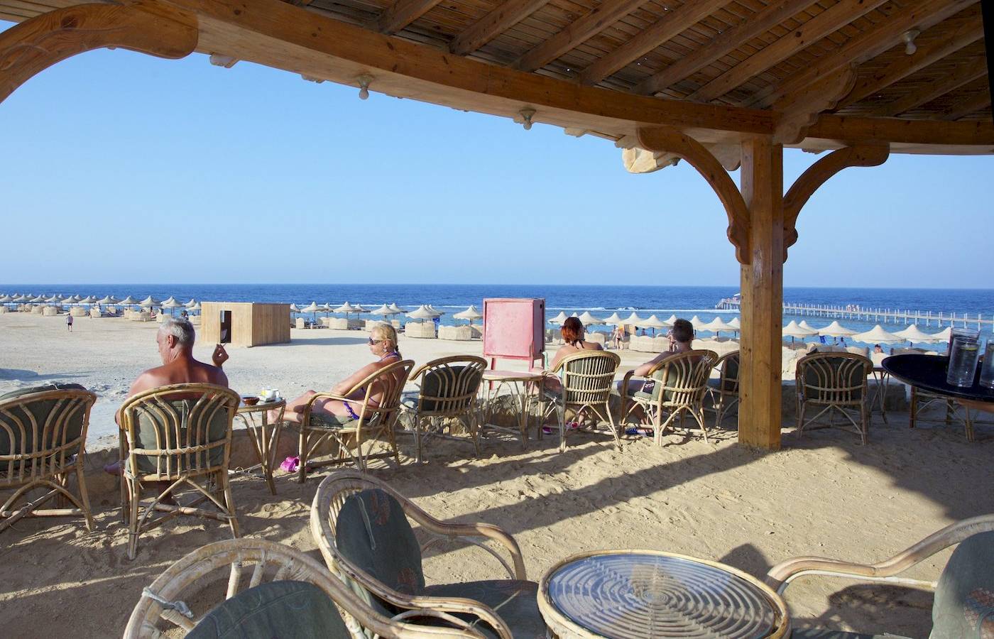 Gäste sitzen unter einem Pavillon am Strand des Three Corners Happy Life Beach Resorts.